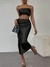 Mulher usando um vestido preto elegante com detalhes em corrente, segurando uma bolsa preta, destacando um estilo moderno.