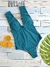 Traje de baño entero color verde con lazos, acompañado de naranjas y hojas verdes sobre un fondo de madera clara.  Ideal para curvas y busto grande.