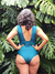 Mujer de espaldas usando un traje de baño enterizo color verde, con un diseño sencillo, frente a un fondo de hojas verdes tropicales. trajes de baño elegantes y funcionales