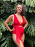 Modelo posando con un corpiño rojo y fucsia, de estilo moderno, en un entorno tropical con plantas verdes.