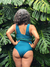 Mujer de espaldas con traje de baño verde, posando entre hojas verdes tropicales.