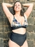 Mujer sonriente usando un corpiño Capri de terciopelo con estampado floral y un bikini de cintura alta negro, posando frente a una pared de piedra.