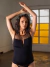 Mujer posando con un top negro de tul plumetti, en un ambiente iluminado con ventanas. Su cabello es rizado y lleva los brazos levantados.