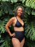 Modelo luciendo un corpiño de bikini negro con detalles azules, en un entorno natural con plantas verdes.