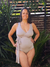 Mujer posando con un traje de baño enterizo color nude, con un diseño envolvente y un lazo en el bajo busto, rodeada de vegetación.