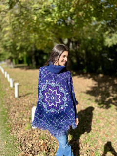 Poncho Mandala azul con diseño mandálico en tonos lilas y blancos, con flecos en el borde, usado por una mujer sonriente en un parque con hojas secas en el suelo