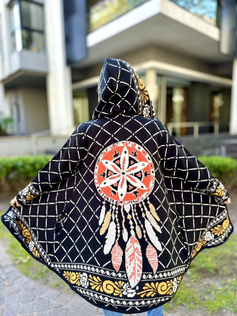 Persona de espaldas usando un sacón con capucha y diseño de atrapasueños en tonos negro, rojo, blanco y amarillo