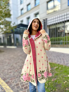 Saco largo con capucha beige con detalles florales rosas y verdes, combinado con un interior rosa, usado por una mujer sonriente en un entorno urbano