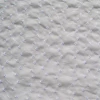 Tela de broderie blanca con bordados en forma de flores sobre fondo blanco.