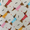 Lona estampada con dibujos de perros salchicha vestidos con suéteres de colores y huesos de perro en un fondo claro.