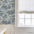 Vinilo estampado Versalles Azul, con un diseño en tonos azul sobre fondo claro, decorando una pared junto a una ventana con cortinas de lino.