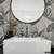 Baño decorado con un vinilo estampado de hojas en tonos grises y un espejo circular.

