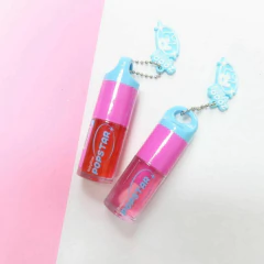 Dos labiales Lip Oil Ruby Rose Popstar en tonos rojo y rosa con tapa azul y rosa, sobre fondo blanco y rosa
