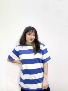 Remera genderless de rayas azul y blanca, con un detalle verde en el cuello, usada por una persona joven.