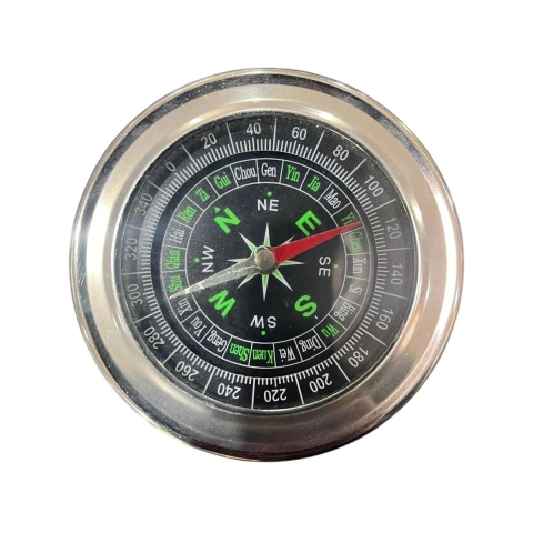 Brújula metálica con fondo negro y números en verde y blanco, con aguja roja y plateada apuntando direcciones cardinales
