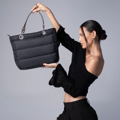 Modelo sosteniendo una bolsa sundar de mano negra con cierre, destacando su diseño moderno y elegante.