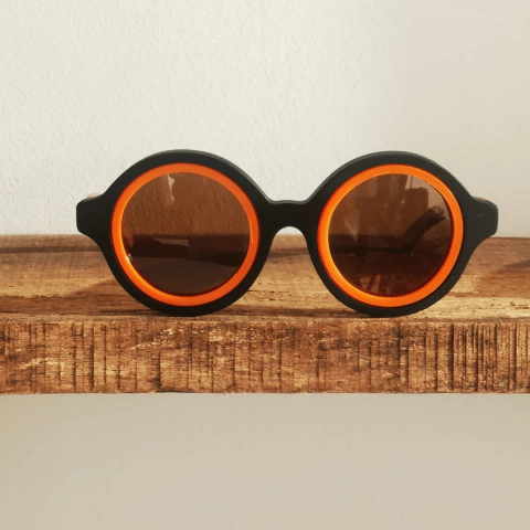 Anteojos de sol de madera y acetato modelo Anthony, con marco negro y detalles naranjas, sobre una mesa de madera.