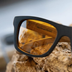 Anteojos de madera y acetato Berna TINT con lentes de color ámbar, sobre una superficie de roca.
