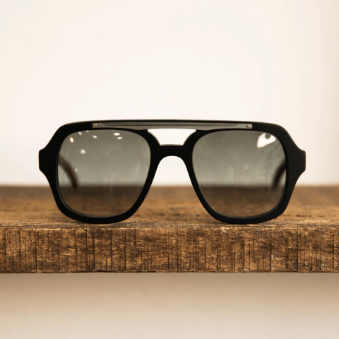 Anteojos de sol de madera, acetato y acero, modelo Barker TINT D, con lentes en color jet black en degradé, sobre una superficie de madera.