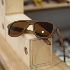 anteojos de sol de madera (patillas) y acetato color marrón rayado oscuro y claro (frente) estilo aviador modelo patagonia marca nomade sobre fondo de madera y blanco