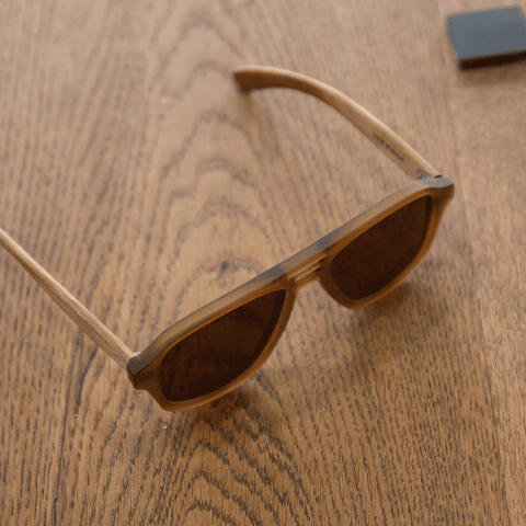 anteojos de sol de madera (patillas) y acetato color marrón rayado oscuro y claro (frente) estilo aviador modelo patagonia marca nomade sobre fondo de madera 