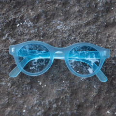 Anteojos Santorini PA TINT D de color azul, con montura transparente, sobre una superficie de piedra.