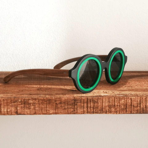Anteojos de sol de madera y acetato modelo Anthony, con montura negra y detalles verdes, sobre una superficie de madera.