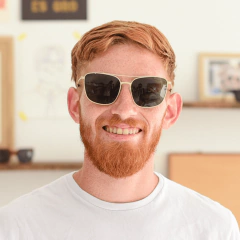 hombre joven de piel blanca, pelo y barba de color rojizo sonriendo con anteojos de sol de metal estilo rectangular con puente y barral modelo La Juanita marca Nomade