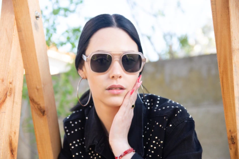 Mujer luciendo anteojos de madera (patillas) y acetato (frente) color rosa traslúcido tipo aviador con lentes de sol polarizados modelo Barker marca Nómade 
