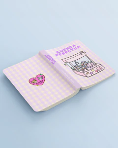 Agenda perpetua A6 con tapa blanda ilustrada en tonos lilas y beige a cuadros, con dibujo de una máquina de garra y texto "Agenda Perpetua"