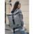 Mochila Arya gris, modelo moderno, llevada por una mujer con chaqueta, en un entorno urbano.