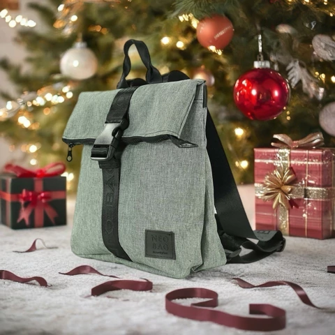 Mochila Mini Arya color gris claro con cierre negro, colocada frente a un árbol de Navidad decorado y regalos envueltos
