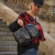 Mujer sosteniendo una mochila negra con un diseño acolchado, vistiendo un suéter rojo y negro, en una escalera al aire libre.