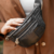 Riñonera Venecia de color negro, con cremalleras y logotipo NEO BAG, sostenida por una mujer con una chaqueta marrón.