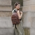 Mochila Luna Bomber en color marrón, llevada por una mujer de espaldas, con un vestido largo y gafas de sol, en un entorno urbano.