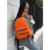 Mochila Luna Bomber en color naranja, llevada por una mujer con chaqueta gris y blusa blanca.