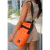 Bolso Matero en Bomber color naranja, con diseño acolchado y correa negra, usado por una mujer en un entorno urbano.