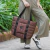 Cartera Melisa marrón, tipo shopper bag, sostenida por una mujer mientras camina por un sendero rodeado de vegetación.