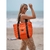 Cartera Melisa de color naranja, con asas negras, llevada por una mujer en la playa.