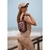 Una mujer sonriente usando un neceser de diseño animal print en la playa, con un atuendo dorado y gorra.