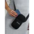 Portacelular Niní negro colgado del hombro, sosteniendo un teléfono móvil en la mano de una persona con uñas pintadas.