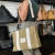 Cartera Tote tela reciclada en color dorado con tiras blancas, llevada por una mujer