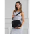 Modelo sosteniendo una bandolera negra de neoprene llamada Sakura, con un vestido gris claro en un fondo neutro.