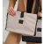 Bolso con sobre porta notebook en color beige, sostenido por una mujer con uñas largas y pintadas, sobre un fondo neutro.