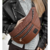 Riñonera Venecia color marrón con cremalleras, llevada por una mujer con chaqueta de cuero negra y blusa a rayas.