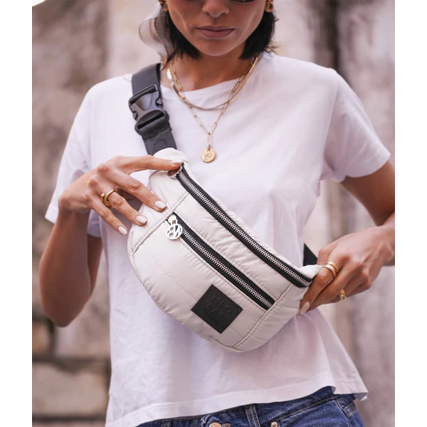 Primer plano de mujer con remera blanca usando riñonera Venecia color blanco crema con cierres negros