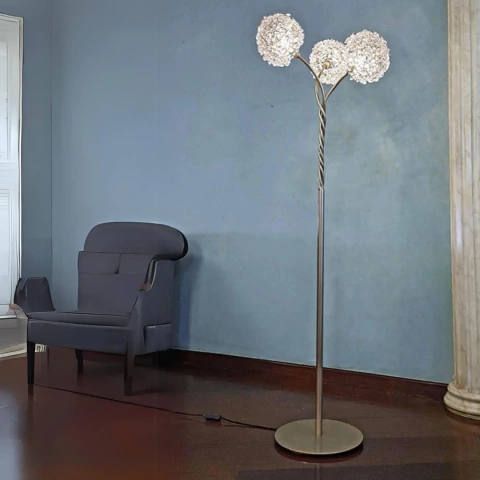 Coluna de cristal castanha Dente de Leão Iris de 140cm, com três cúpulas decorativas, posicionada em sala de estar moderna ao lado de uma poltrona preta.