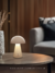 Luminária abajur cinza Mush da Sindora em uma mesa de centro, com design moderno e bateria recarregável. Comprar Lustres Online é na Lustres Gênesis. A Maior e melhor empresa para comprar Lustres do Brasil
