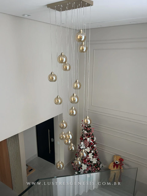 Lustre pendente Sarvah com 21 globos conhaque, instalado em hall de entrada com pé direito duplo e decoração natalina ao fundo.