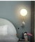 Arandela moderna em formato de astronauta escalando na parede de um quarto, com luz dourada brilhando acima de uma cama com cabeceira branca. Lustres Genesis loja online de Lustres e Iluminação Decorativa